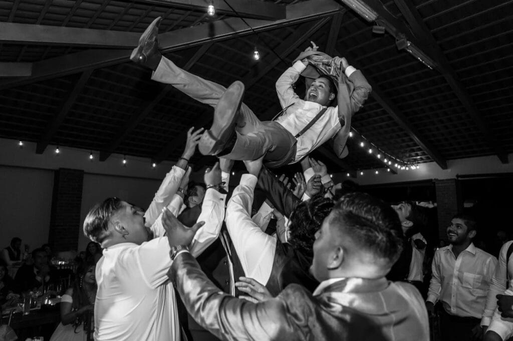 A jubilant group of men lifting a friend in celebration during a lively indoor party.